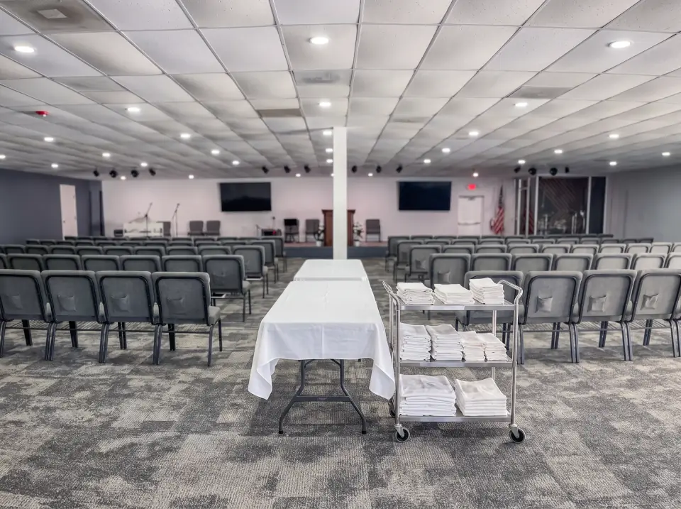 Folding tables with white cloths set in the Sacred Farewells room, a cart of linens beside them