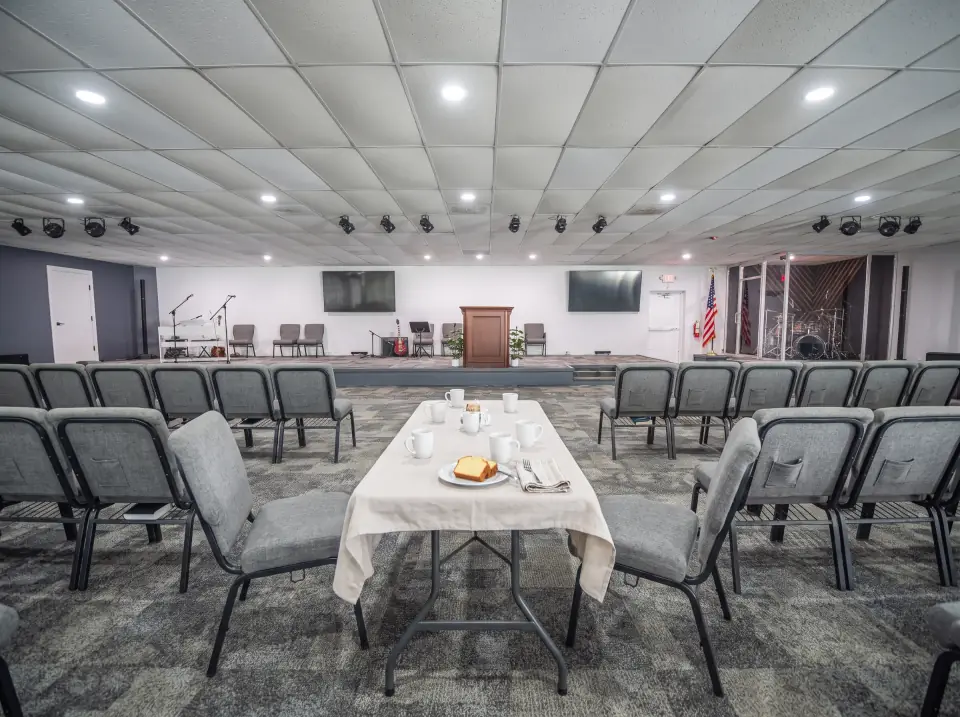 A cloth-covered table with coffee cups and a slice of pound cake near the front of the Sacred Farewells hall